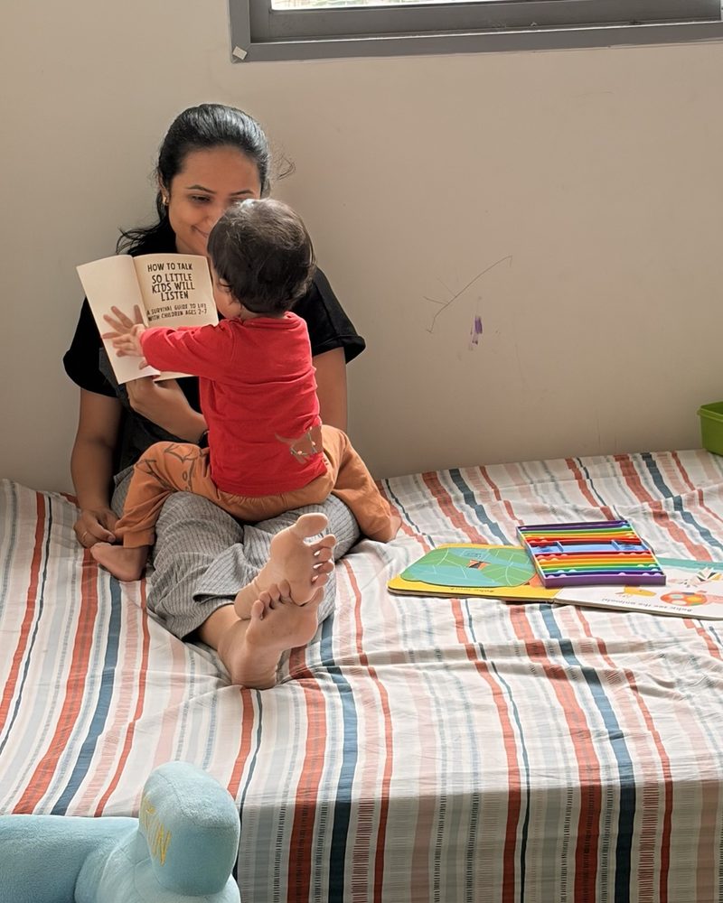 Manali reading a parenting book with her baby on her lap